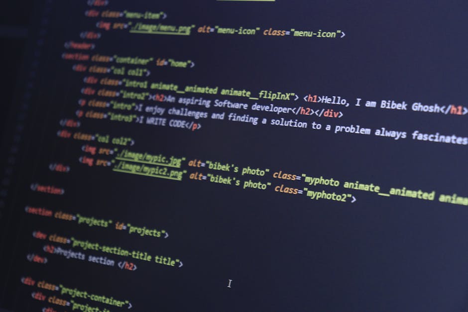 A pair of hands actively use a laptop placed on a dark surface, with the screen displaying lines of computer code in a dark-themed editor. The person's fingers rest on the keyboard, and the background