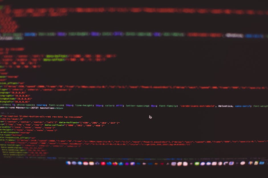 Close-up of a computer screen displaying lines of code in various colors, including red, green, and purple, on a black background. The code appears to be HTML or CSS, with elements such as tags, attri